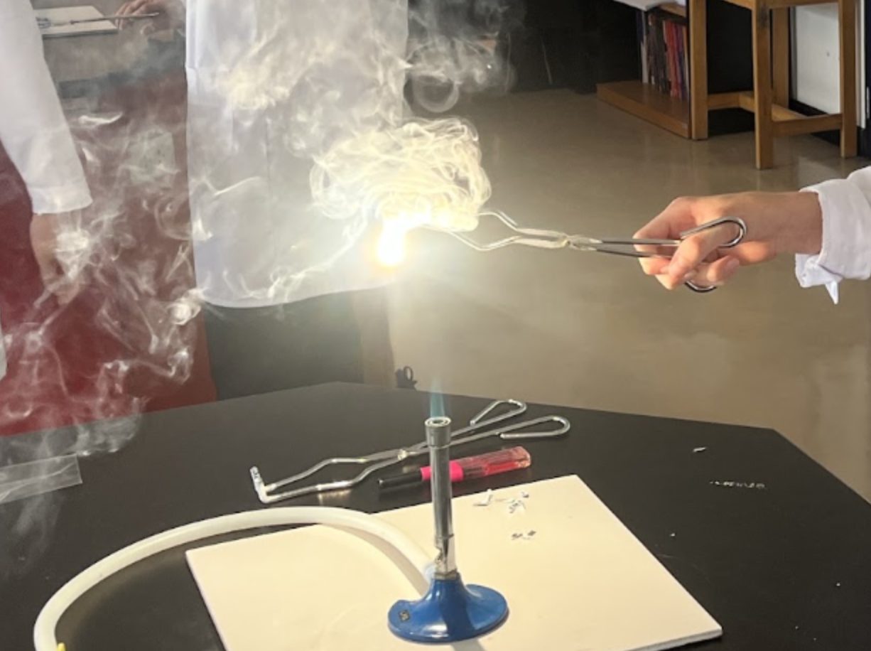A student holding magnesium ribbon over a Bunsen burner flame